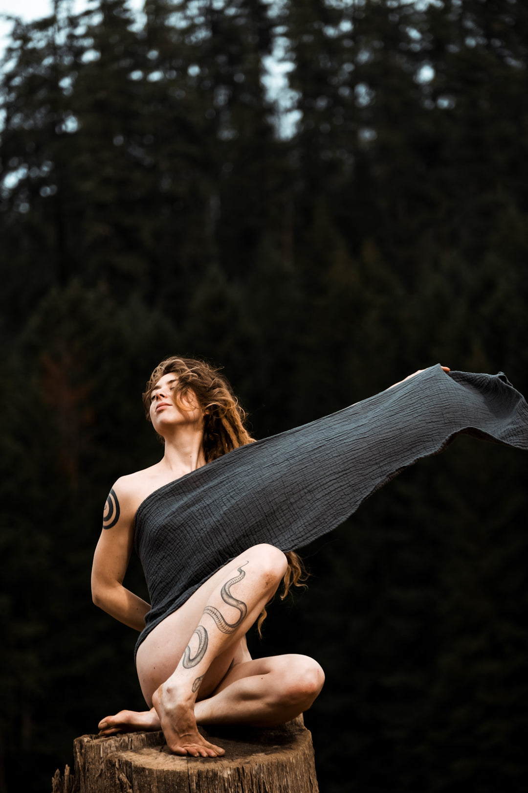 Female model sits on a tree stump with long gauze wrap stretched out covering her body.