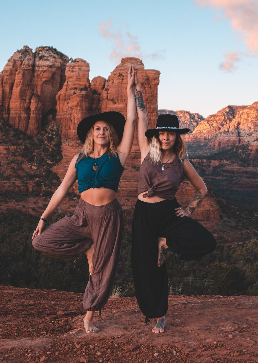 Two women are posed together wearing blousy yoga pants, tank tops and cowboy hats.