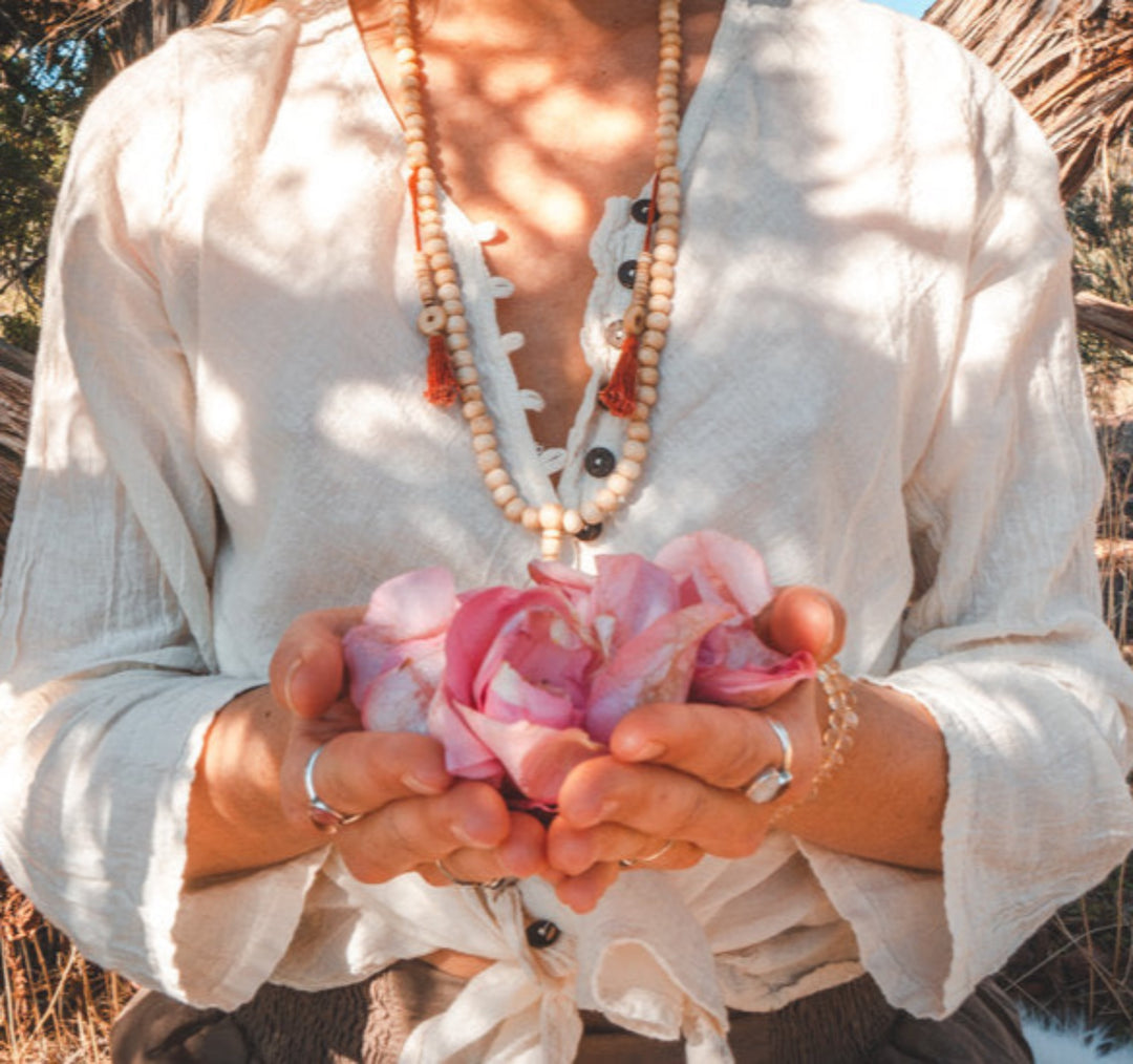 Model is wearing un-dyed gauze shirt with buttons. She holds rose petals in her palms.
