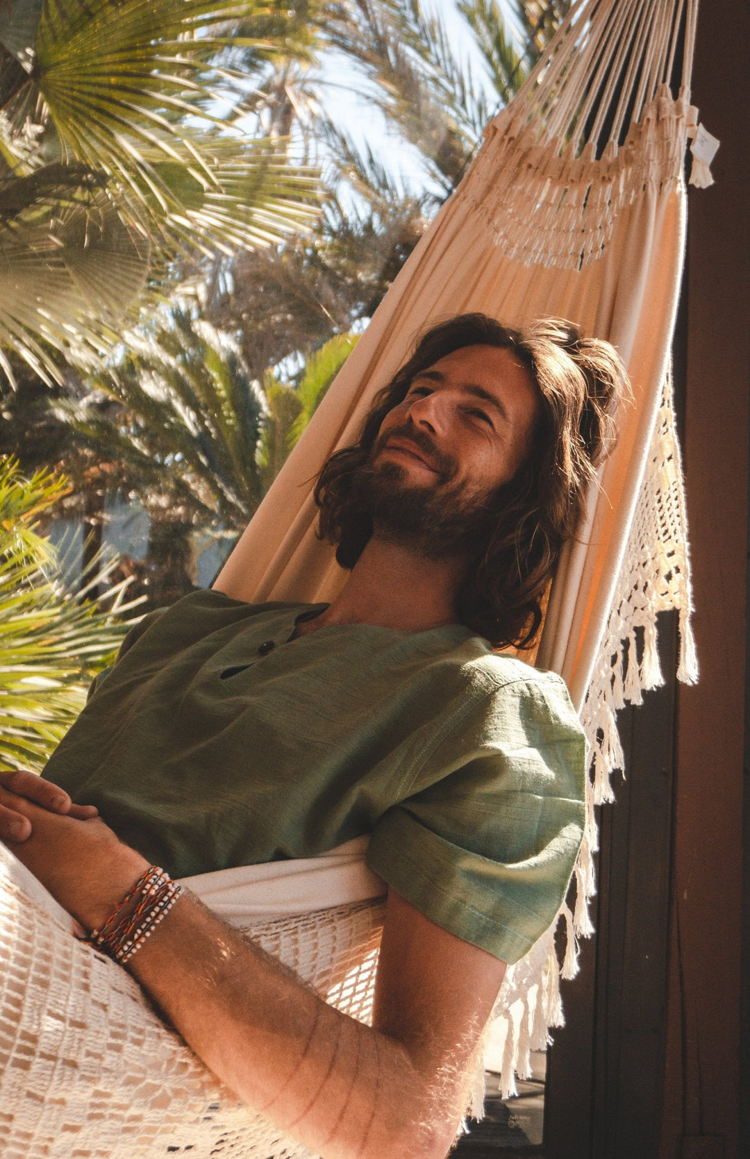 Male model relaxes in hammock wearing green shirt.