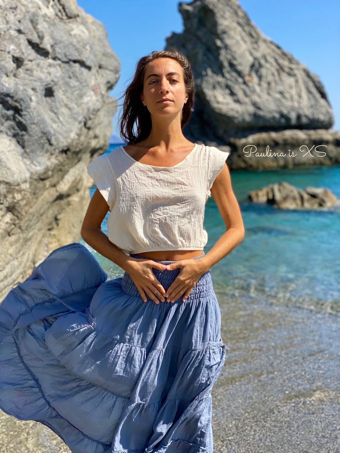 Woman model on beach wearing un-dyed crop top and flowing periwinkle skirt.